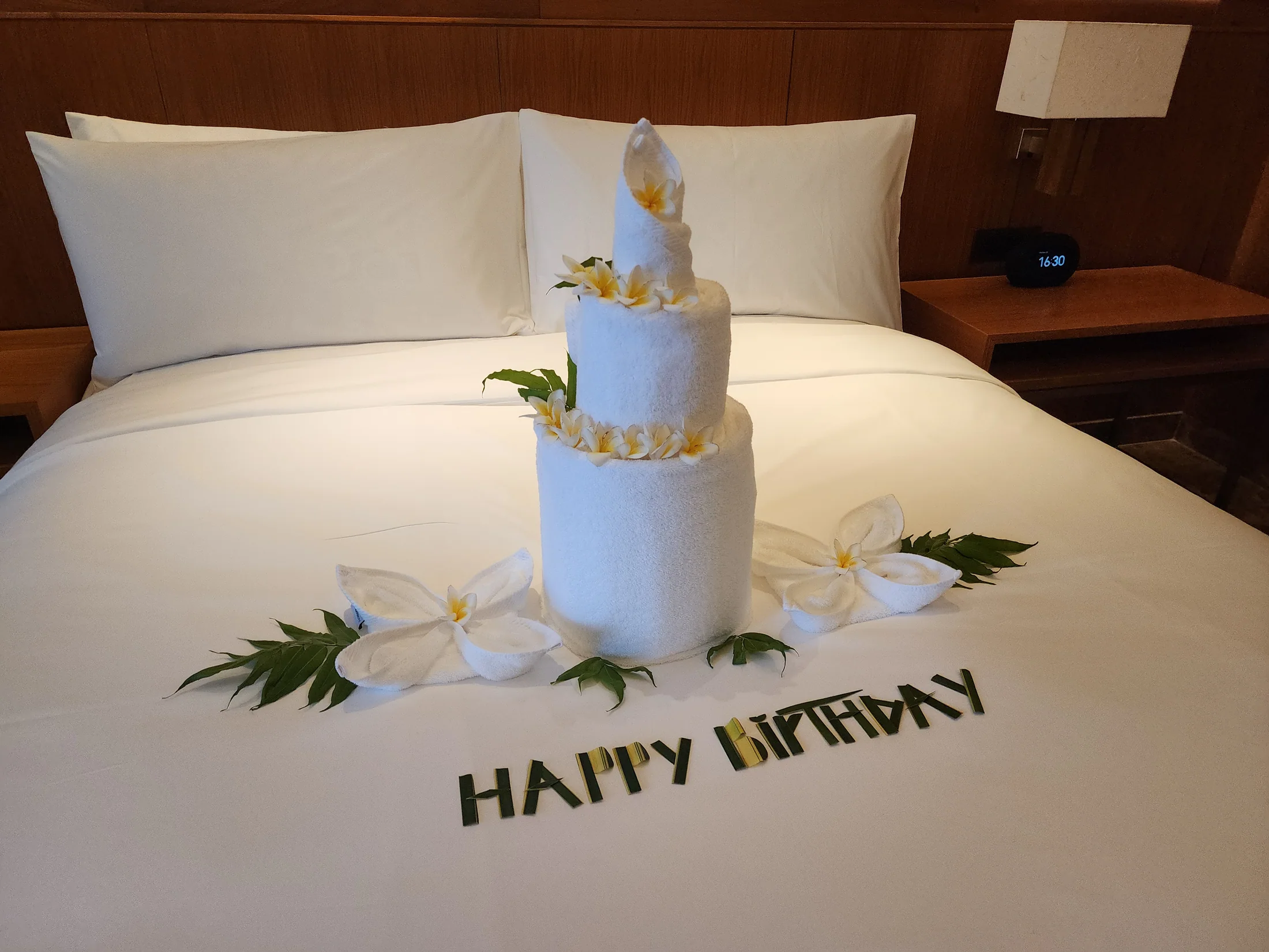 Happy birthday 문구와 케이크 모양의 타월 장식이 놓인 침대